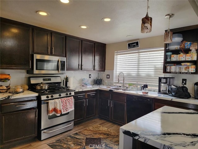 kitchen with dark brown cabinetry, stainless steel appliances, sink, pendant lighting, and light hardwood / wood-style floors