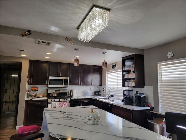 kitchen featuring appliances with stainless steel finishes, light stone counters, sink, hardwood / wood-style floors, and hanging light fixtures