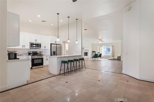 kitchen featuring stainless steel appliances, ceiling fan, decorative light fixtures, white cabinets, and a breakfast bar area