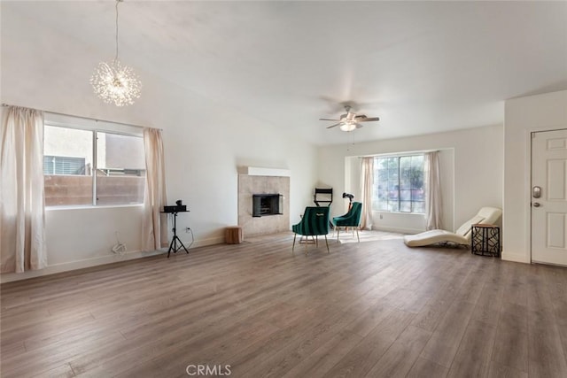 unfurnished living room featuring a tile fireplace, hardwood / wood-style floors, and ceiling fan with notable chandelier