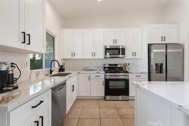 kitchen featuring appliances with stainless steel finishes, vaulted ceiling, sink, white cabinets, and light tile patterned flooring