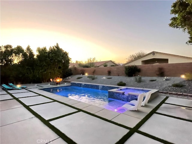 pool at dusk with an in ground hot tub and a patio