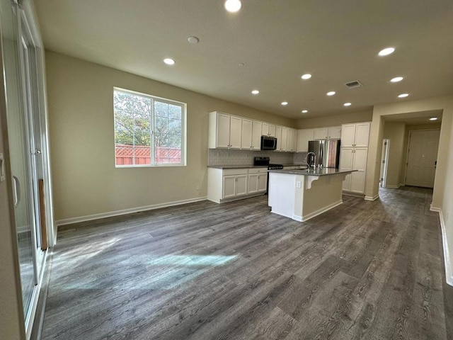 kitchen featuring dark wood-type flooring, white cabinetry, stainless steel appliances, tasteful backsplash, and a kitchen island with sink