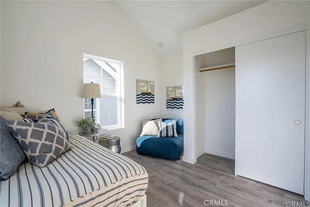 bedroom with vaulted ceiling, light wood-type flooring, and a closet