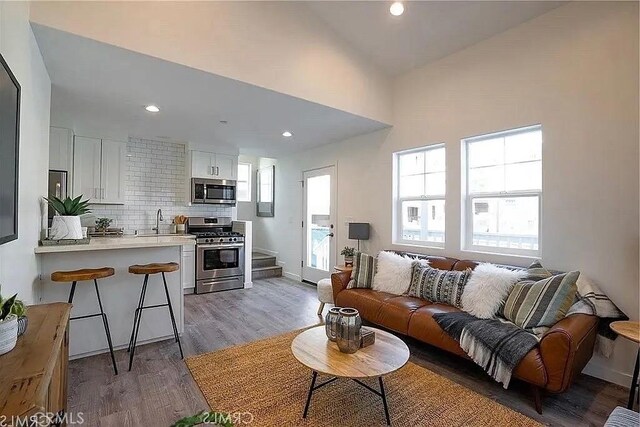 living room featuring light hardwood / wood-style floors, lofted ceiling, and sink