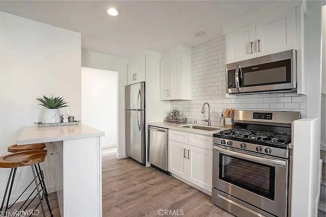 kitchen featuring white cabinetry, sink, a kitchen breakfast bar, light hardwood / wood-style flooring, and appliances with stainless steel finishes