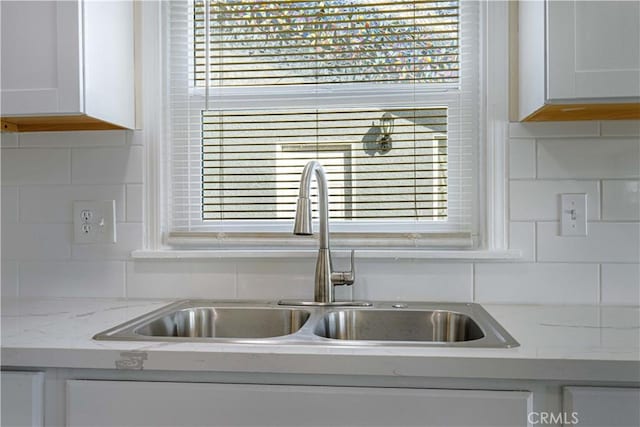 details featuring light stone countertops, white cabinetry, decorative backsplash, and a sink