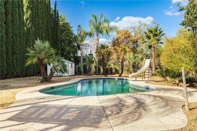 pool featuring a shed, a patio, a water slide, and an outdoor structure