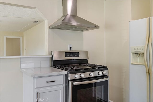 kitchen with wall chimney exhaust hood, white refrigerator with ice dispenser, white cabinets, and gas stove