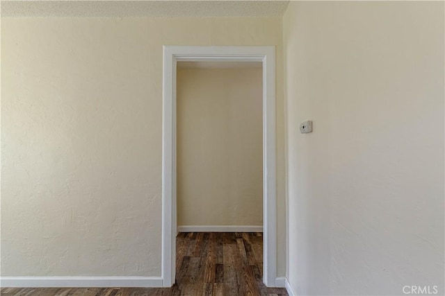 corridor with dark wood-type flooring and baseboards