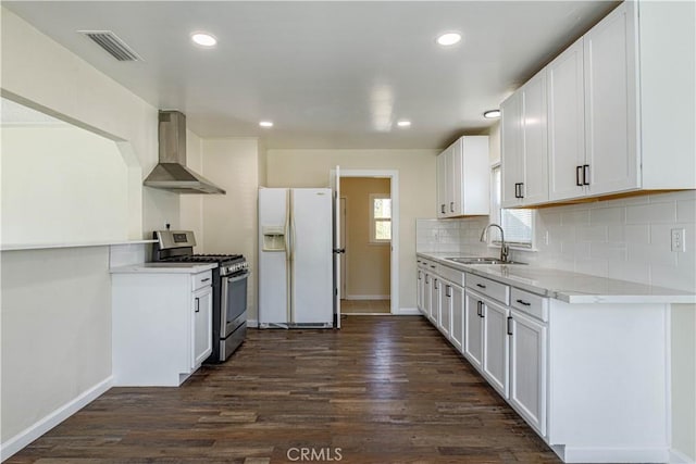 kitchen with white refrigerator with ice dispenser, a sink, white cabinets, wall chimney exhaust hood, and gas range