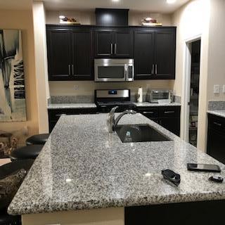 kitchen featuring sink, an island with sink, light stone counters, and range