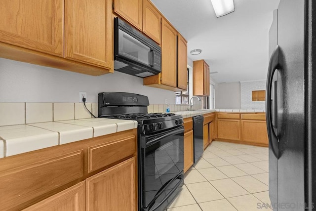 kitchen featuring black appliances, light tile patterned floors, sink, and tile countertops