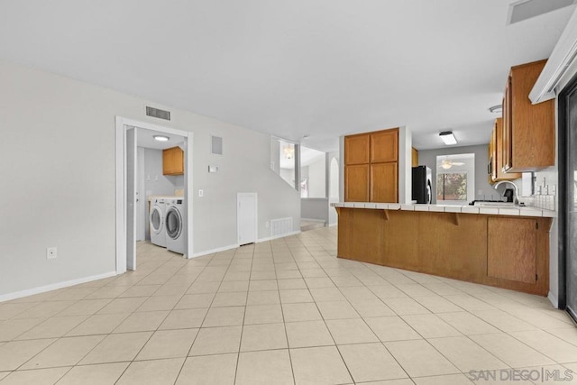 kitchen with kitchen peninsula, black fridge, washer and dryer, light tile patterned floors, and tile countertops