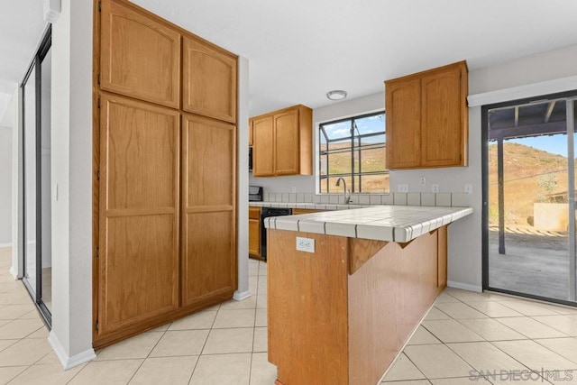 kitchen with tile countertops, dishwasher, kitchen peninsula, and light tile patterned floors