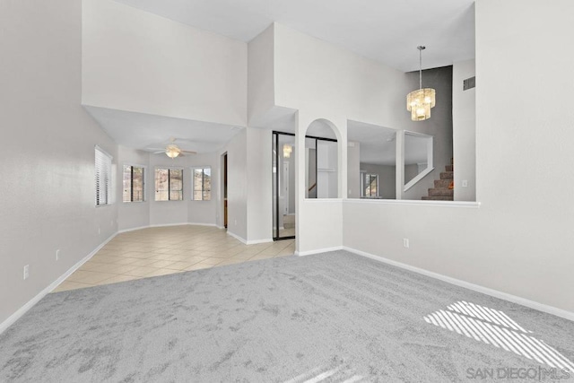 unfurnished living room featuring ceiling fan with notable chandelier, a towering ceiling, and light carpet