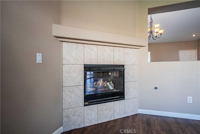 details with a tiled fireplace, a notable chandelier, and hardwood / wood-style flooring