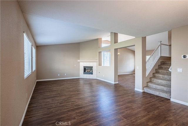 unfurnished living room with a tile fireplace, vaulted ceiling, and dark wood-type flooring