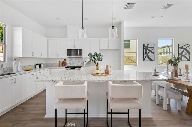 kitchen with a center island, dark wood-type flooring, white cabinets, decorative light fixtures, and stainless steel appliances