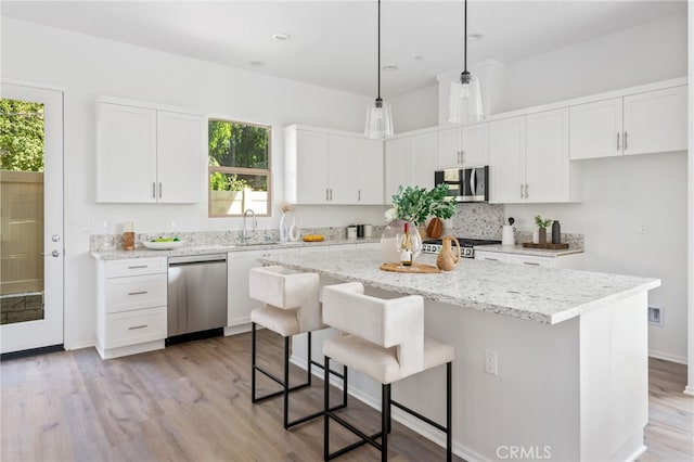 kitchen with appliances with stainless steel finishes, a kitchen island, pendant lighting, light hardwood / wood-style flooring, and white cabinetry