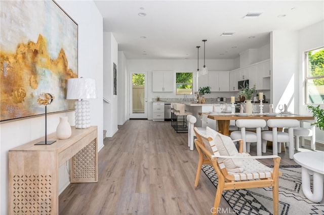 interior space featuring light wood-type flooring, stainless steel dishwasher, a breakfast bar, pendant lighting, and white cabinets