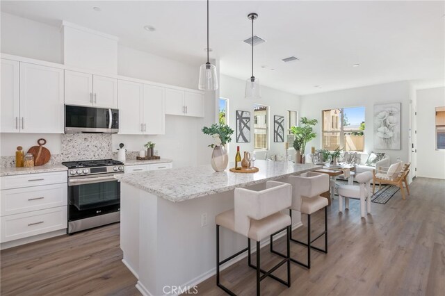 kitchen featuring white cabinets, a center island, stainless steel appliances, and hanging light fixtures