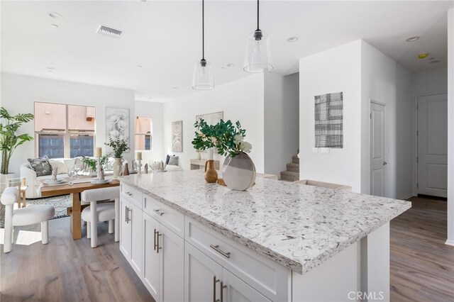 kitchen featuring white cabinets, light hardwood / wood-style flooring, decorative light fixtures, a kitchen island, and light stone counters