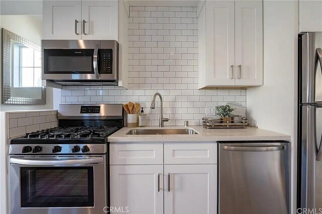 kitchen featuring light stone countertops, backsplash, stainless steel appliances, sink, and white cabinets