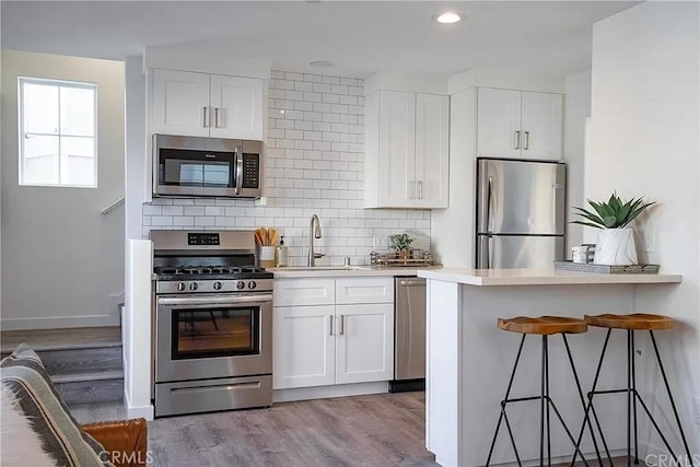 kitchen with white cabinetry, sink, backsplash, appliances with stainless steel finishes, and light wood-type flooring