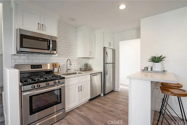 kitchen featuring a kitchen breakfast bar, sink, appliances with stainless steel finishes, light hardwood / wood-style floors, and white cabinetry