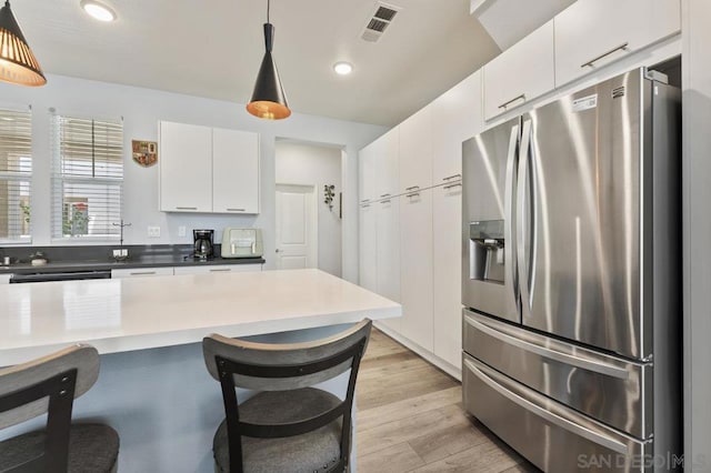 kitchen featuring white cabinets, stainless steel fridge with ice dispenser, light hardwood / wood-style flooring, and hanging light fixtures