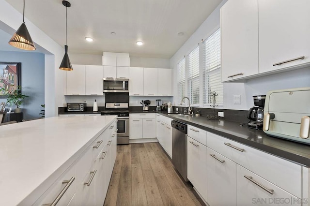 kitchen featuring hanging light fixtures, sink, light wood-type flooring, appliances with stainless steel finishes, and white cabinetry