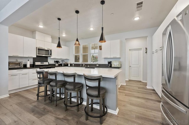 kitchen featuring stainless steel appliances, a kitchen island, pendant lighting, light hardwood / wood-style flooring, and white cabinetry