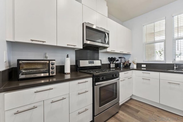 kitchen with appliances with stainless steel finishes, sink, white cabinetry, and hardwood / wood-style floors