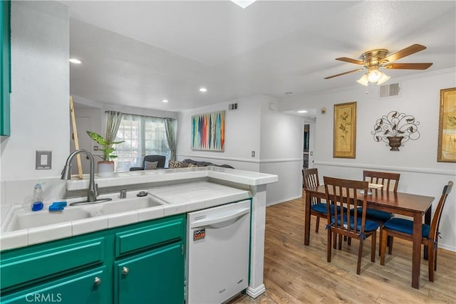 kitchen with light wood-type flooring, ceiling fan, sink, tile countertops, and dishwasher