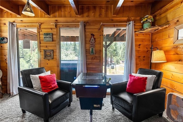 living area featuring beamed ceiling, plenty of natural light, carpet flooring, and wooden walls