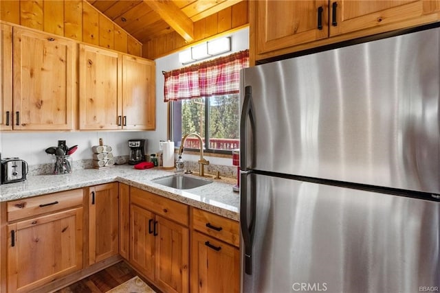 kitchen featuring wooden ceiling, sink, vaulted ceiling with beams, stainless steel fridge, and light stone counters