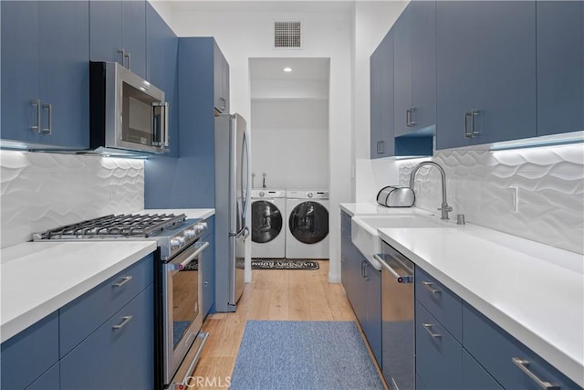 kitchen featuring blue cabinetry, stainless steel appliances, tasteful backsplash, separate washer and dryer, and light hardwood / wood-style flooring