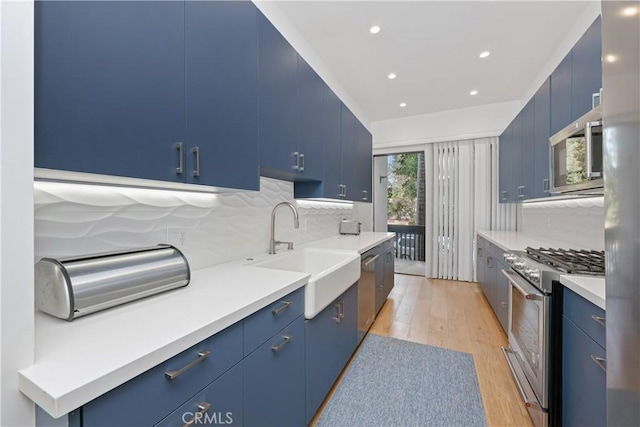 kitchen with sink, light wood-type flooring, blue cabinetry, and appliances with stainless steel finishes