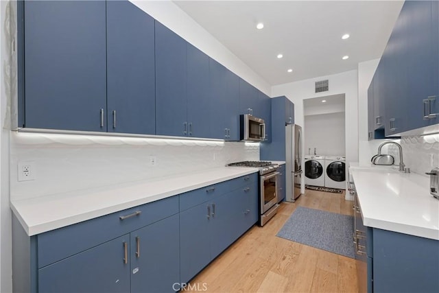 kitchen featuring blue cabinetry, sink, washer and clothes dryer, appliances with stainless steel finishes, and light wood-type flooring