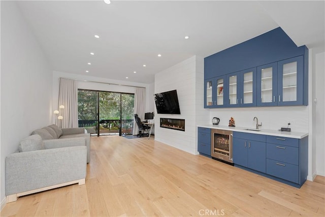 bar with blue cabinetry, sink, wine cooler, a fireplace, and light wood-type flooring