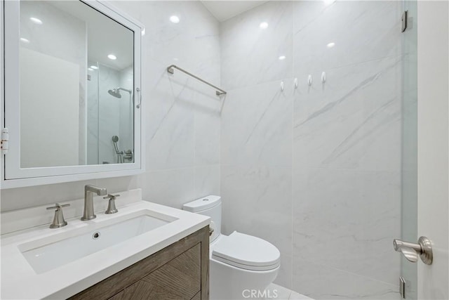 bathroom featuring vanity, toilet, a shower with door, and tile walls