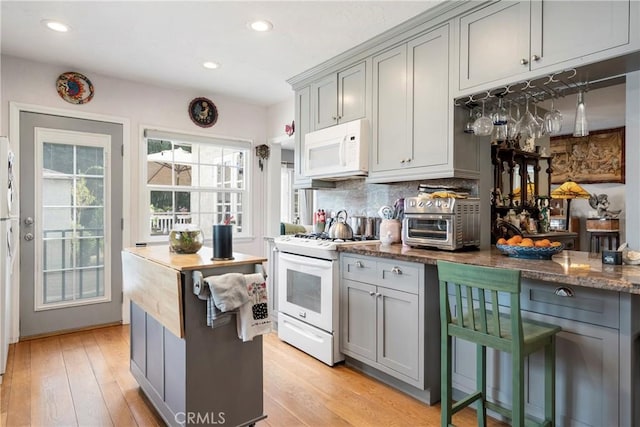 kitchen with gray cabinetry, white appliances, dark stone counters, and light hardwood / wood-style flooring