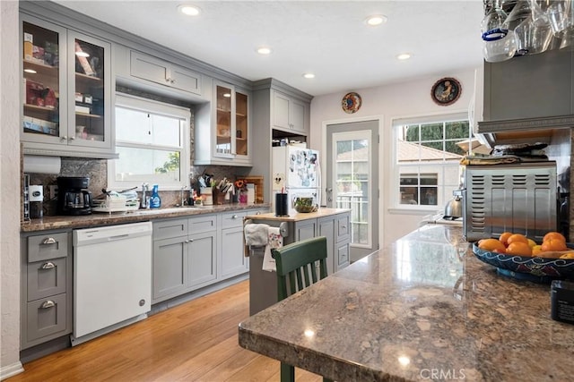 kitchen with gray cabinetry, light hardwood / wood-style flooring, a healthy amount of sunlight, and white appliances