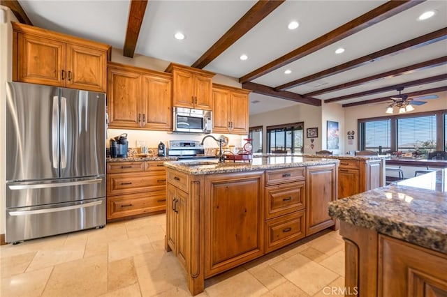 61138 Onaga Trl, Joshua Tree, CA 92252 - kitchen with stainless steel appliances, beamed ceiling, brown cabinets, a kitchen island with sink, and stone counters