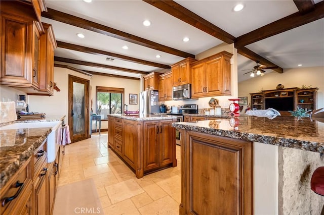 kitchen with ceiling fan, appliances with stainless steel finishes, dark stone countertops, lofted ceiling with beams, and a kitchen island