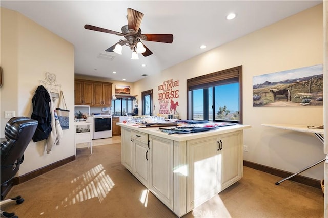 kitchen with washer / dryer, a center island, light carpet, and ceiling fan