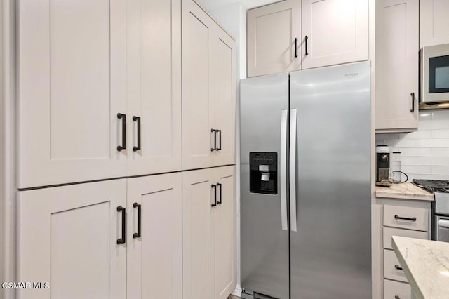 kitchen with light stone counters, appliances with stainless steel finishes, backsplash, and white cabinets