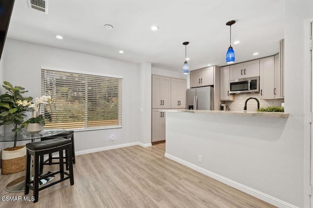 kitchen with kitchen peninsula, pendant lighting, stainless steel appliances, light hardwood / wood-style floors, and decorative backsplash