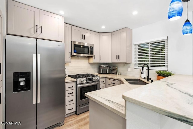 kitchen with appliances with stainless steel finishes, pendant lighting, sink, backsplash, and kitchen peninsula